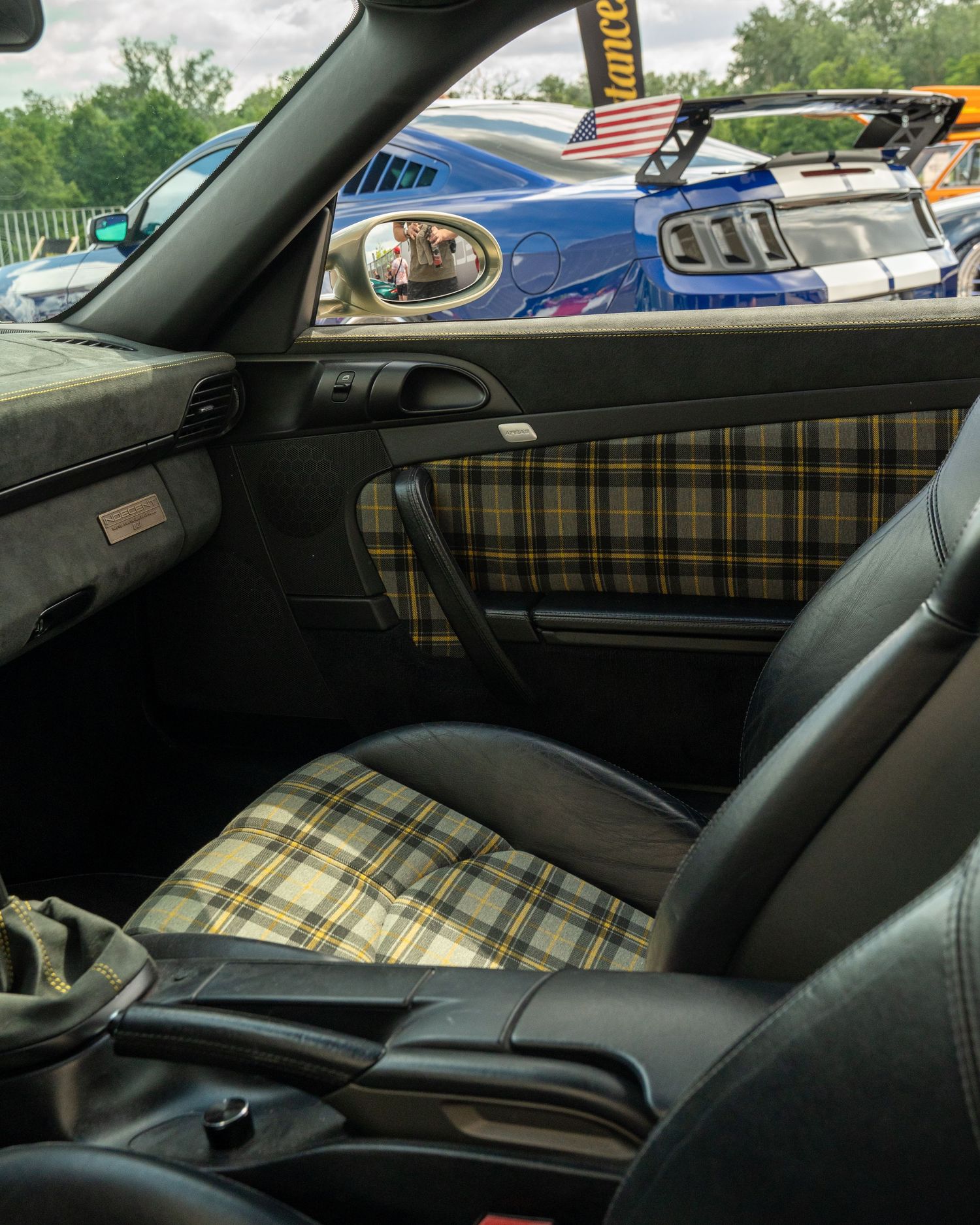 Interior view of a classic car showing plaid upholstery and dashboard details through the passenger side window.