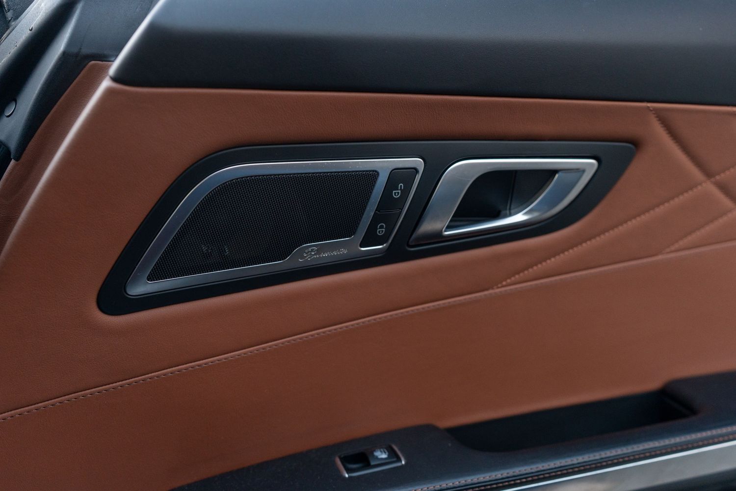 Brown leather interior door panel detail of a luxury vehicle showing sleek design elements.