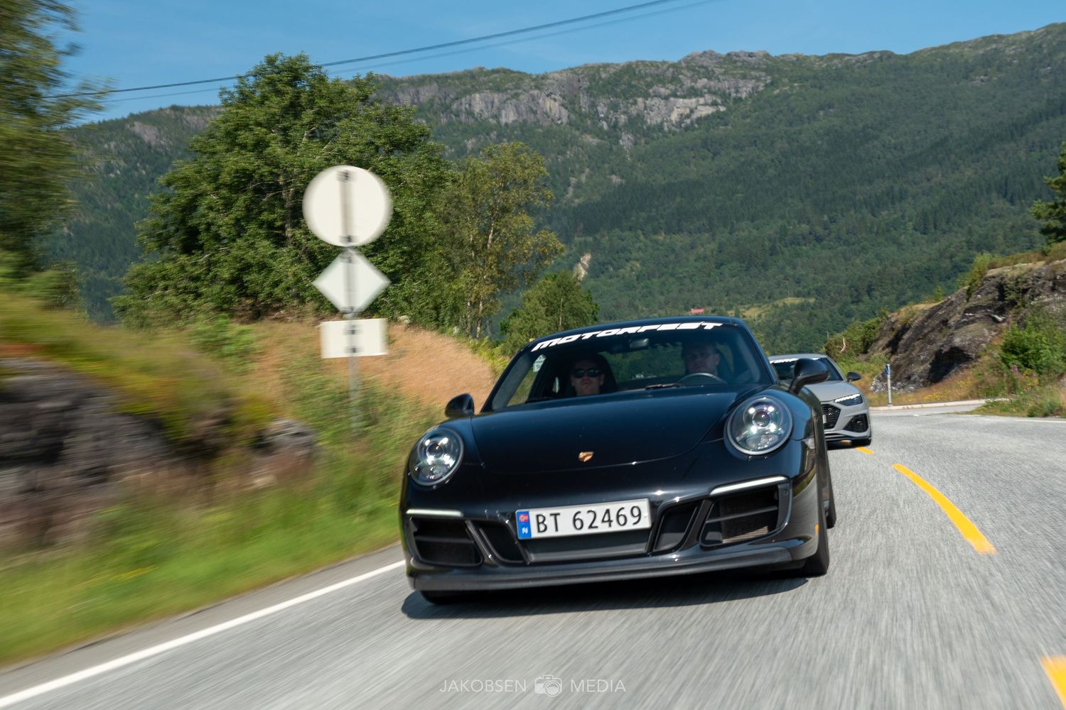 Dark sports cars driving on a winding mountain road with scenic Norwegian landscape.