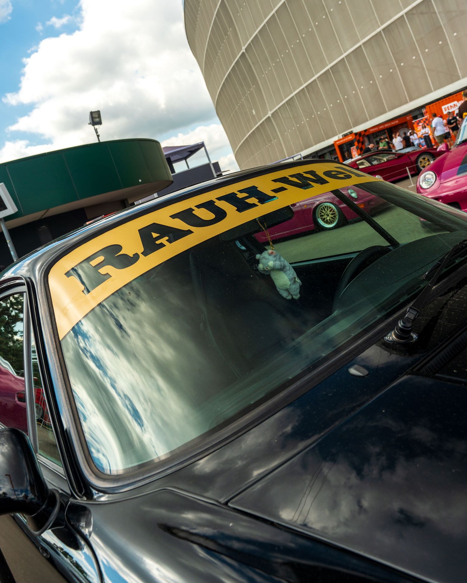 Black car with yellow RAUH-Welt windshield banner photographed at an automotive event.