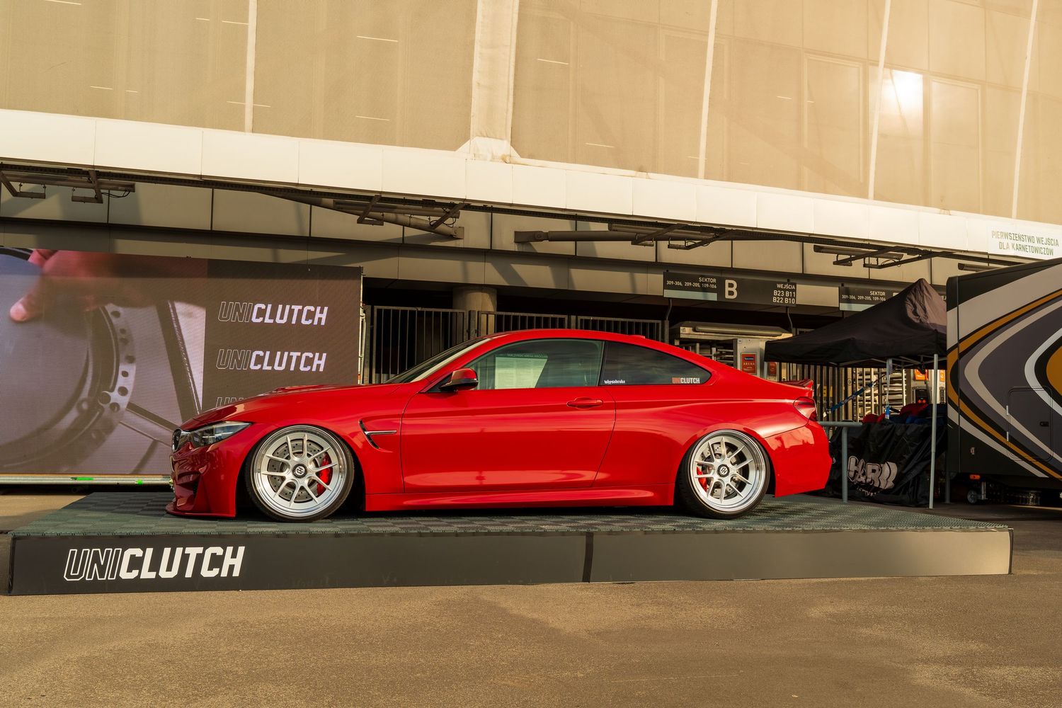 A lowered bright red BMW M4 sports car on stance wheels parked in a parking garage.