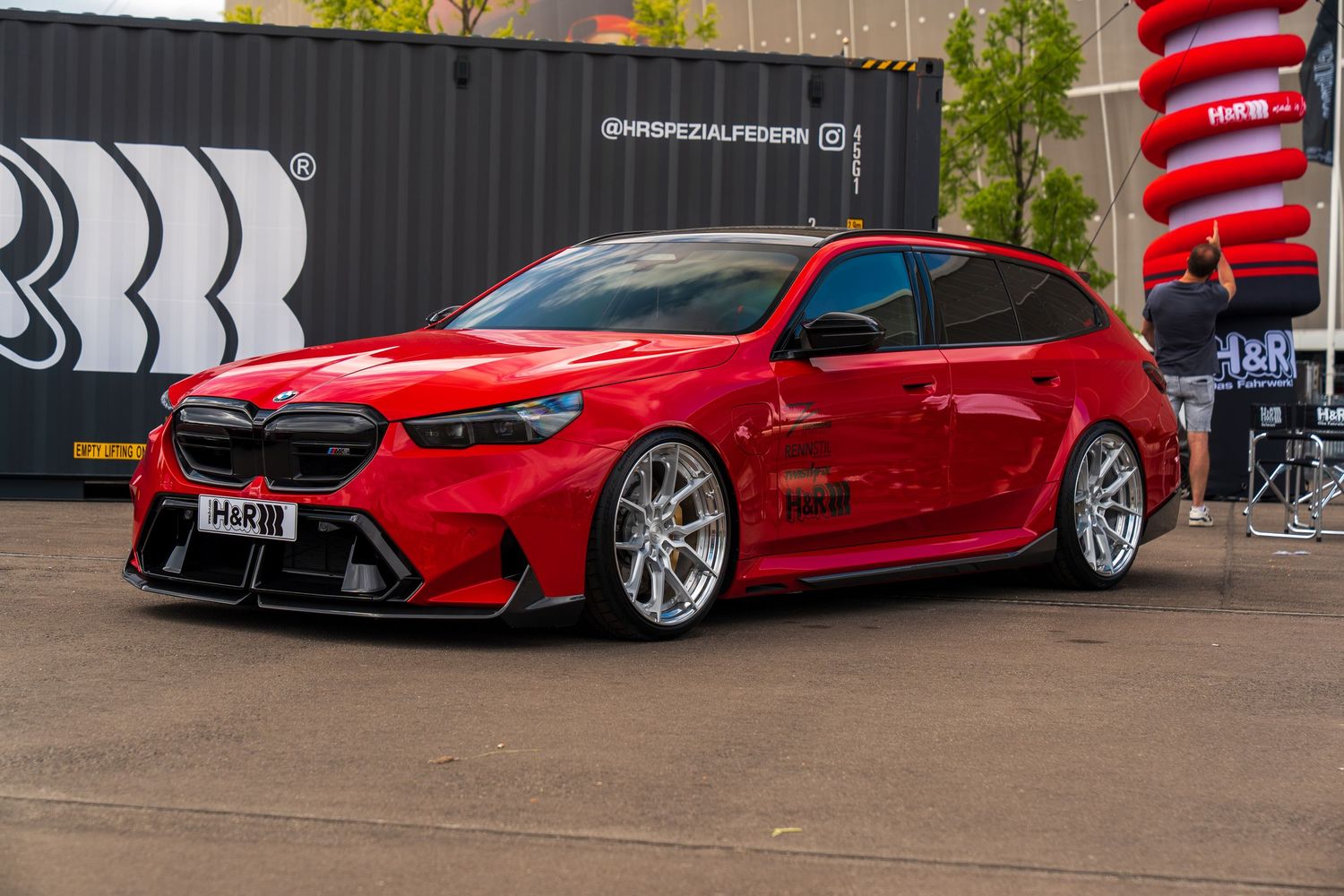 Lowered red BMW M4 Gran Coupe with custom body kit and silver wheels at an automotive event.