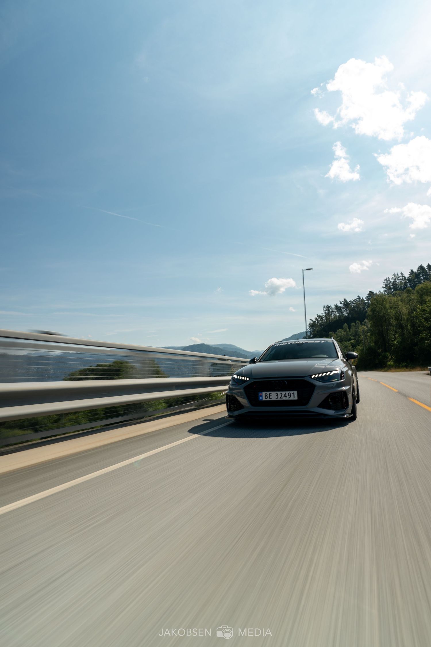 Grey sports car cruising down an empty highway with mountains in the background.