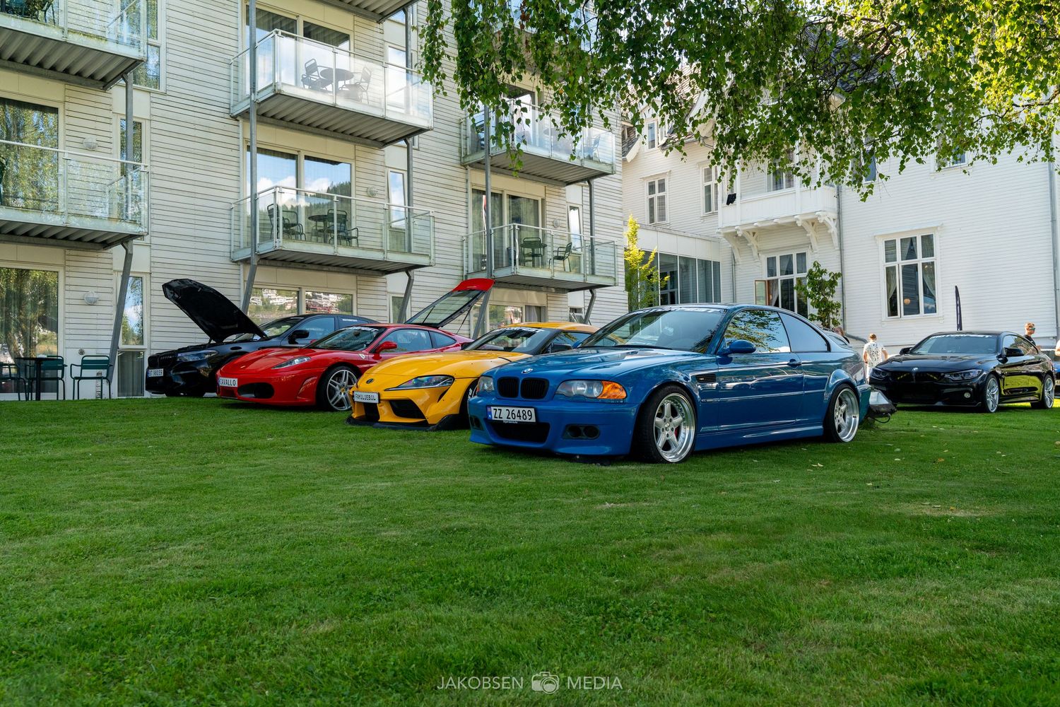 Luxury performance cars parked on a grassy area next to residential buildings.