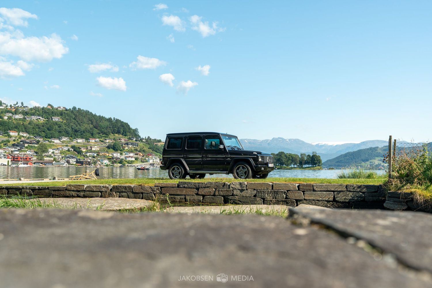 Scenic mountainside parking area with cars overlooking a lake and mountains.