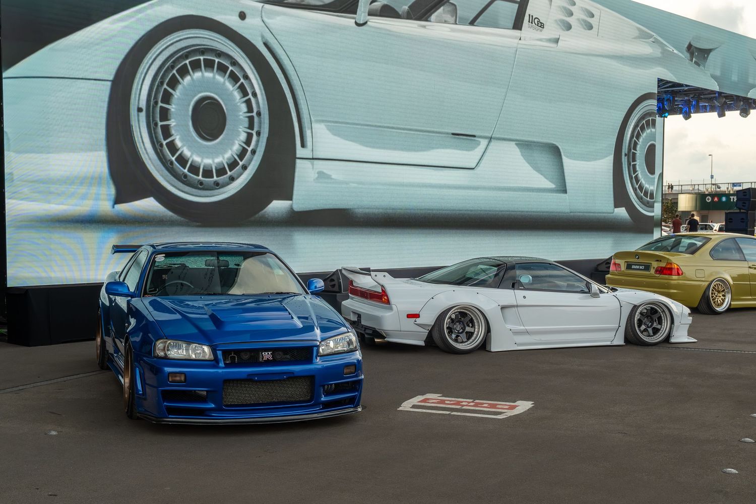 A blue Nissan Skyline GT-R parked next to white sports cars under a large automotive mural.