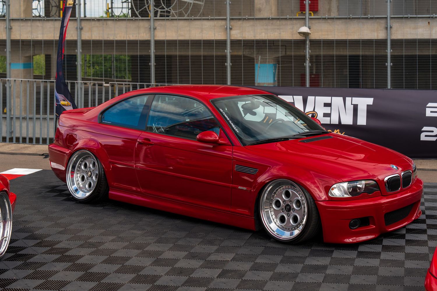 Custom lowered red BMW M3 with modified body kit and aftermarket wheels on display.