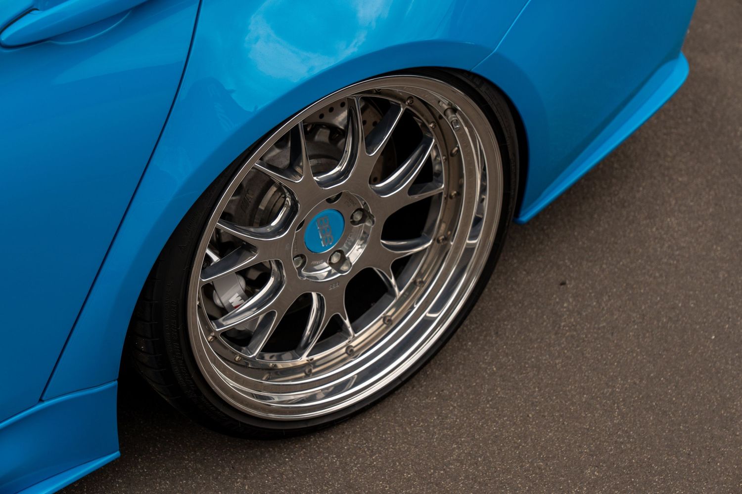 Close-up view of a custom blue BMW M3 wheel with polished multi-spoke rims and low profile tires.
