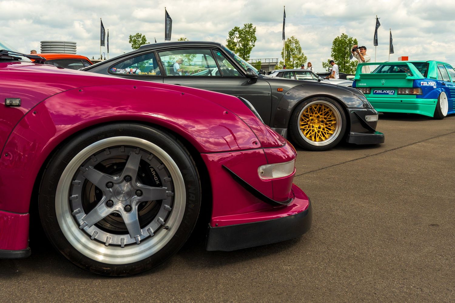 A lineup of colorful JDM sports cars featuring purple, turquoise and gold paint displayed at a car meet.