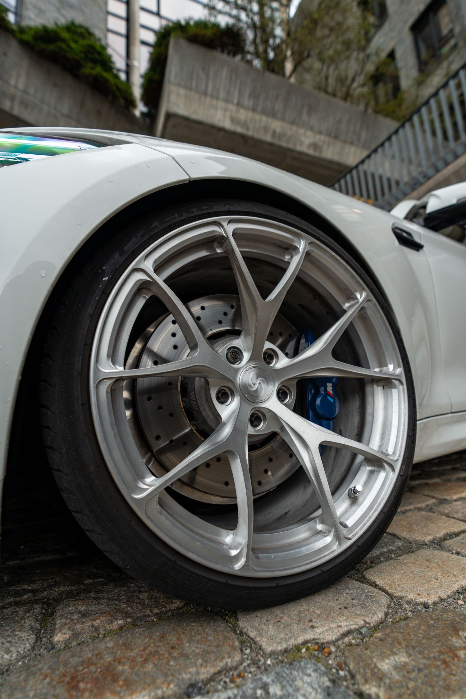 Close-up detail of silver forged wheel and blue brake caliper on white BMW sports car.