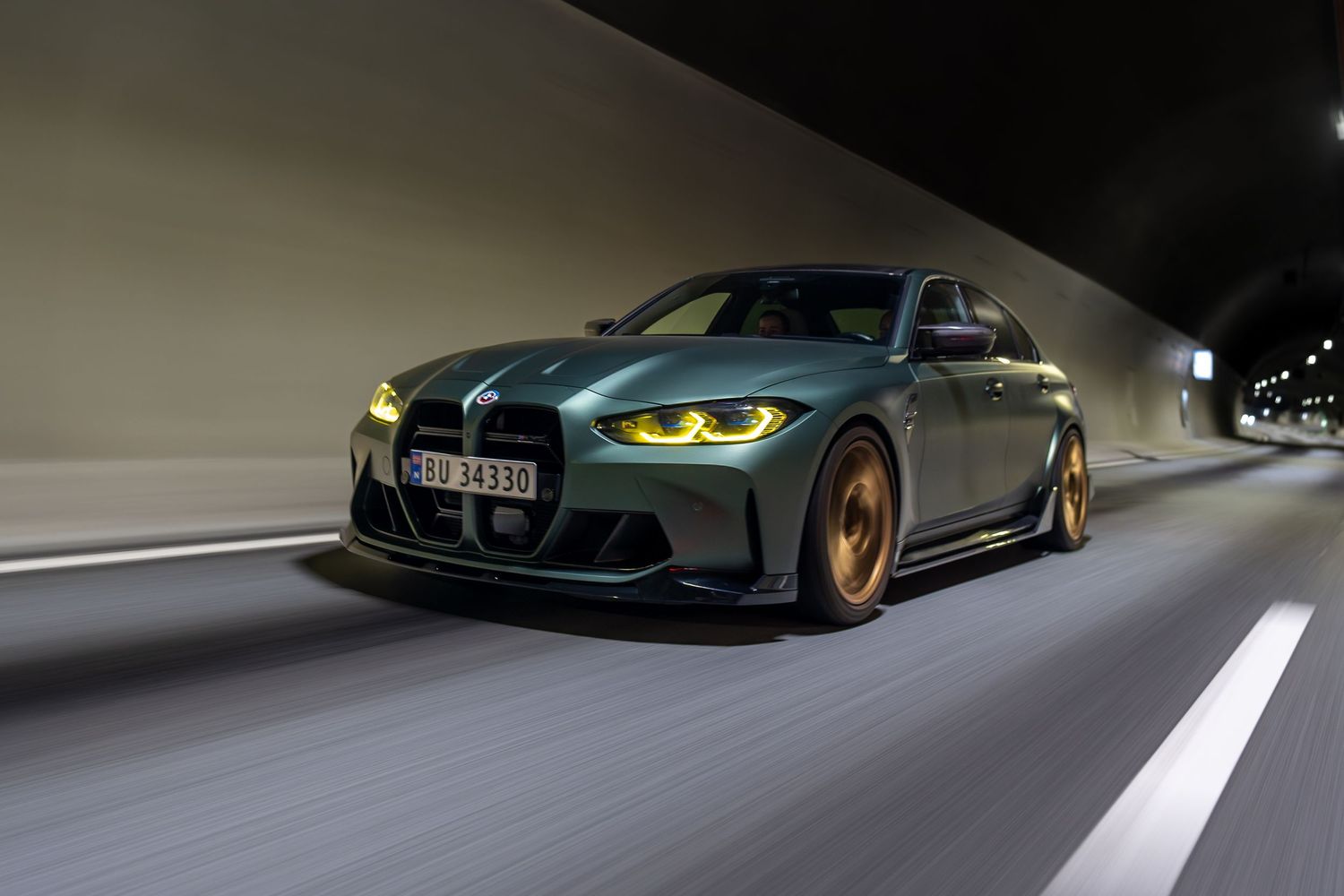 Green BMW M4 with glowing headlights driving through tunnel at night.