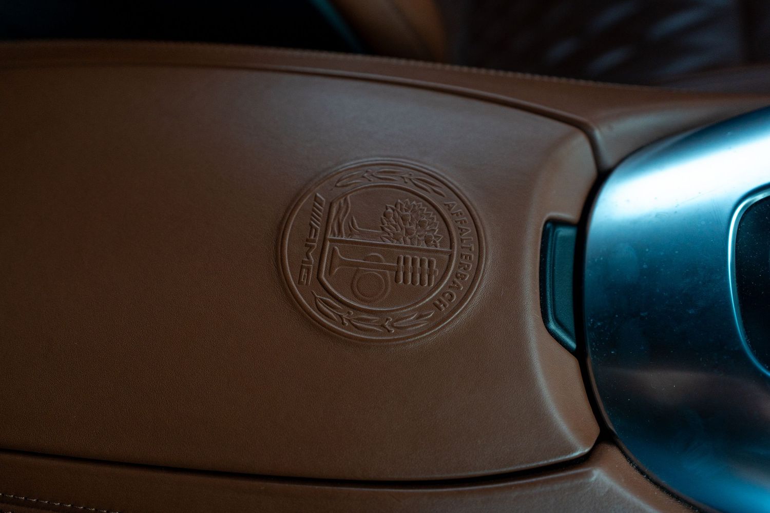 Closeup of an embossed luxury car logo on a leather interior panel with metallic blue accents.