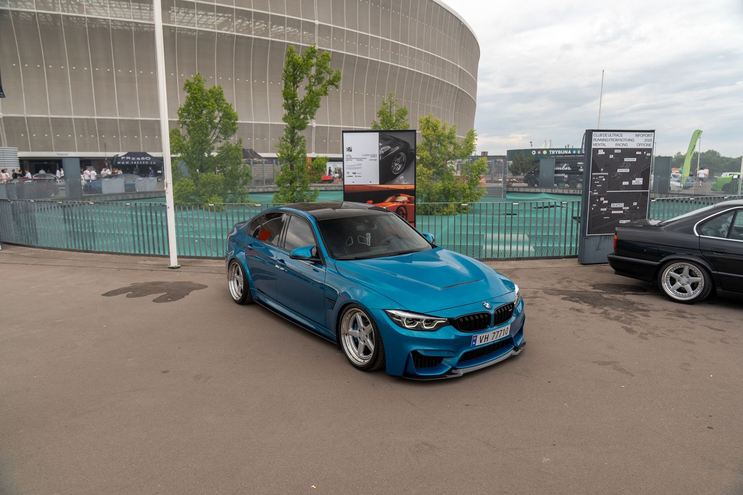 A custom BMW M4 in bright blue showcasing its modified stance and wheels against an industrial backdrop.
