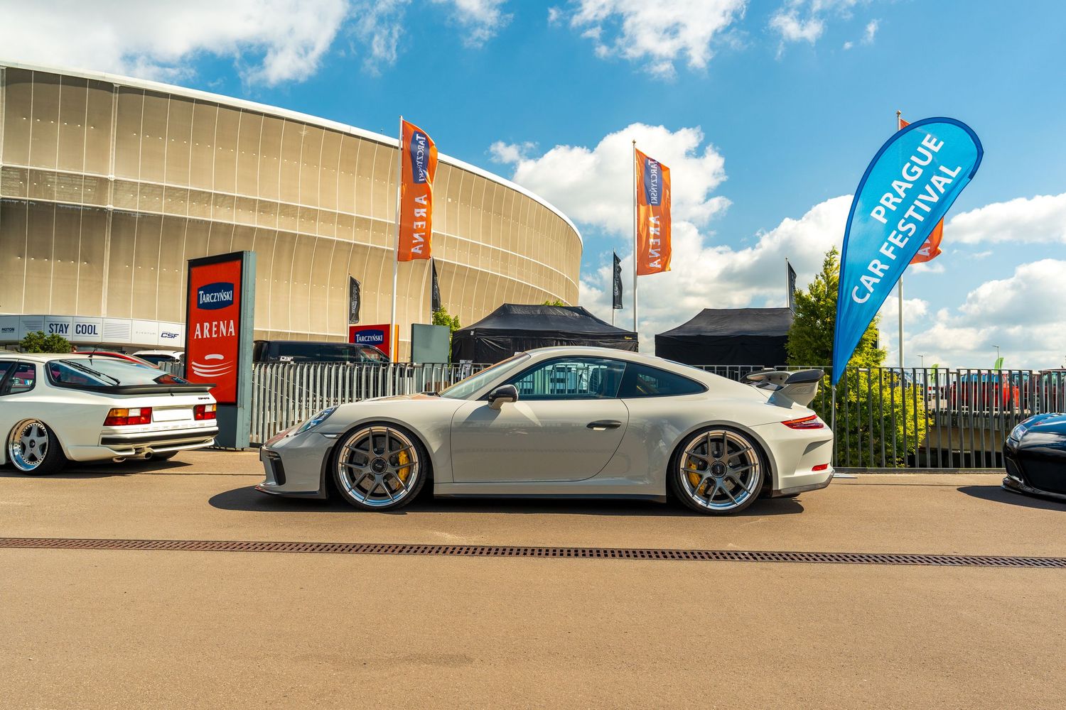 A row of luxury sports cars including Porsche models parked outside a modern building under blue skies.