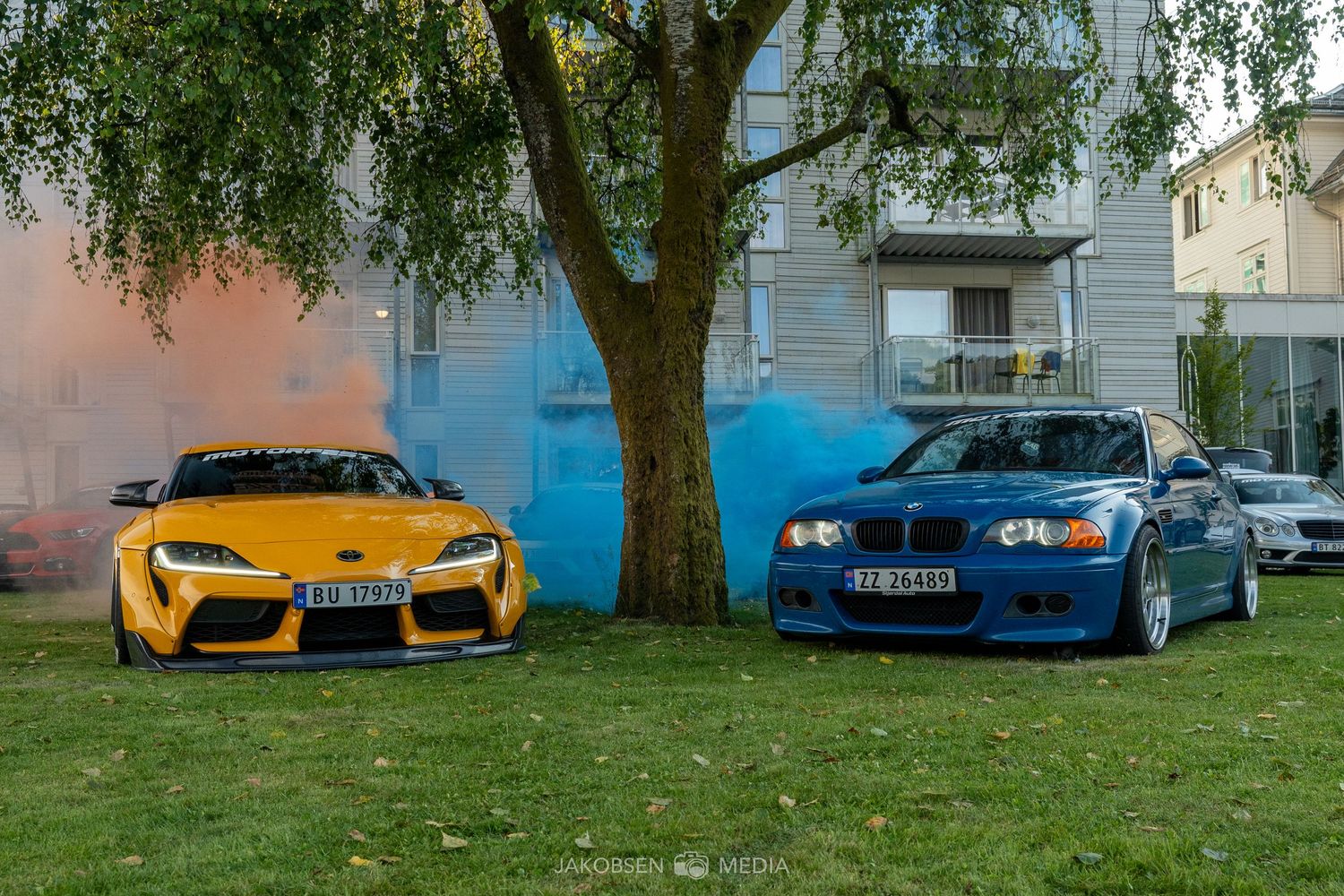 Modern sports cars including BMW and Corvette models displayed on a lawn near residential buildings.