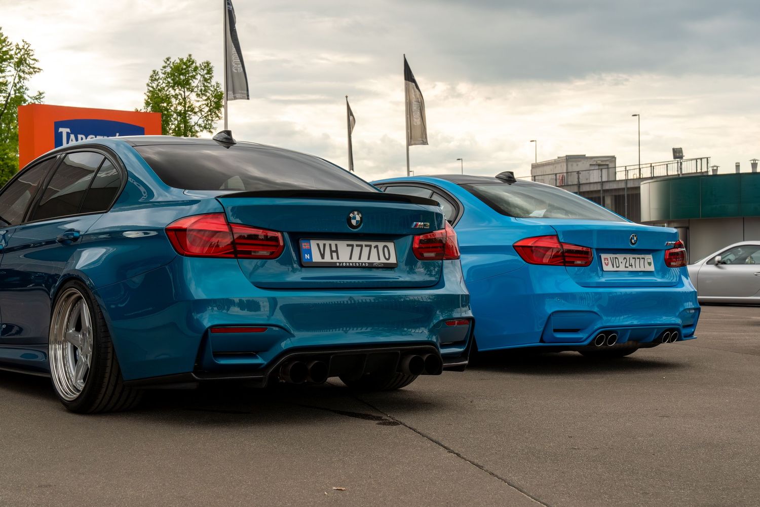 Two BMW M3s in matching metallic blue paint with lowered suspension parked side by side at a car meet.