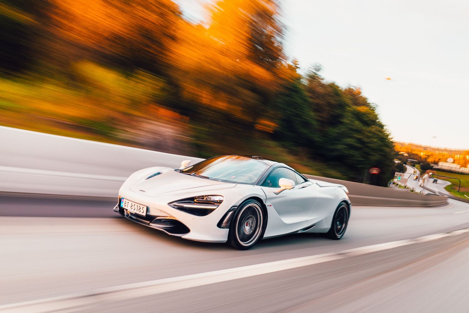 White McLaren 720S in motion on curved road during autumn sunset.
