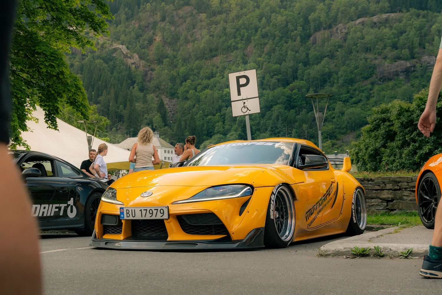 Yellow Toyota Supra widebody stance car parked at a car meet with mountain scenery in Norway.