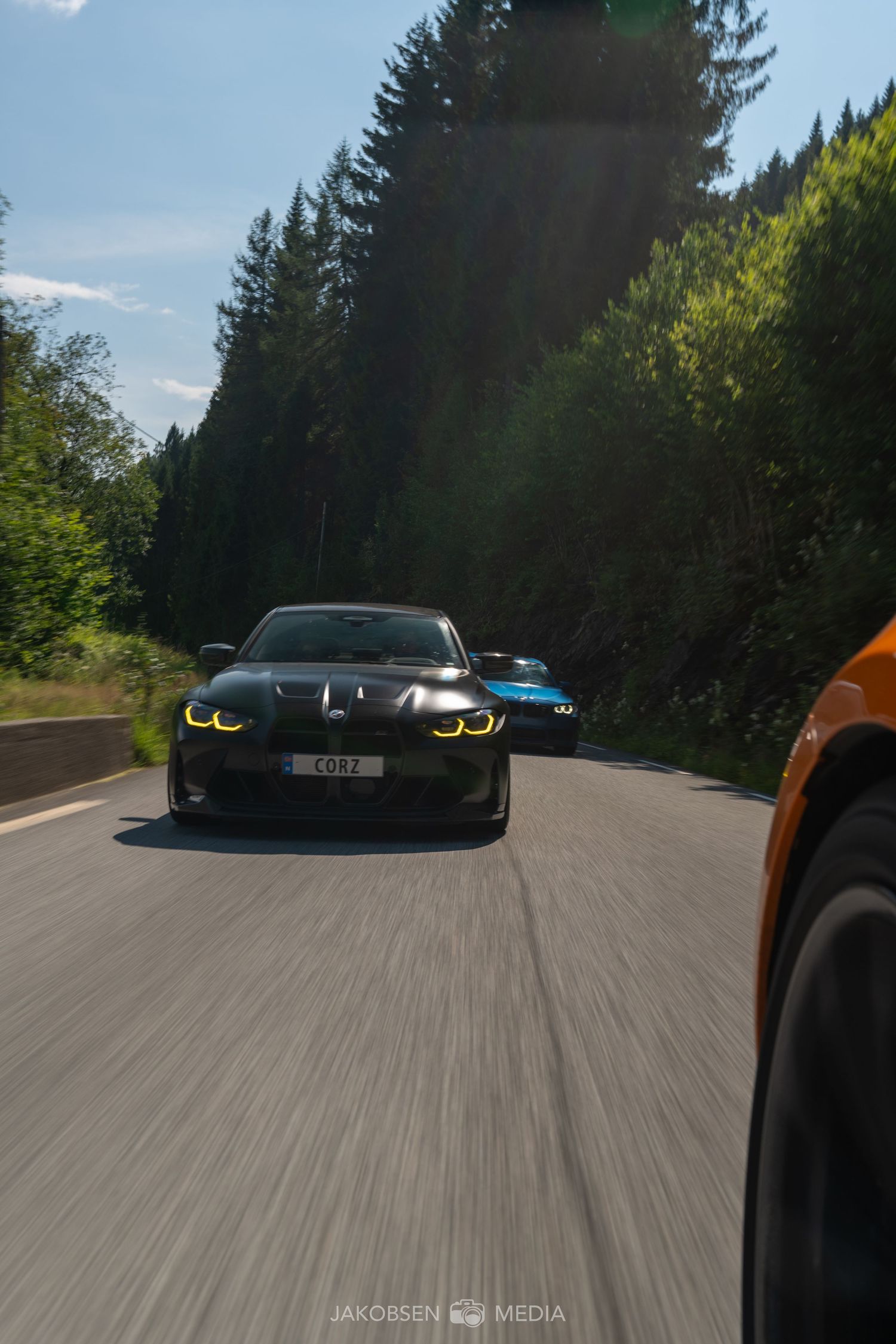 Performance cars driving through a forested road captured from a low action angle.