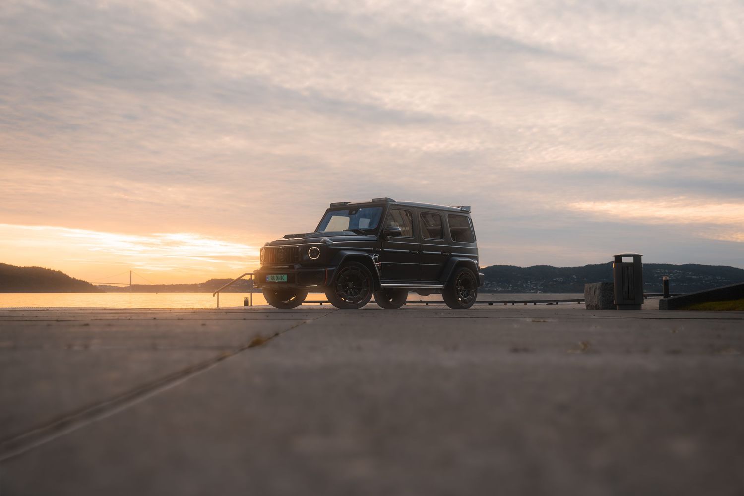 Silhouettes of luxury SUV vehicles lined up against scenic seaside sunset backdrop.