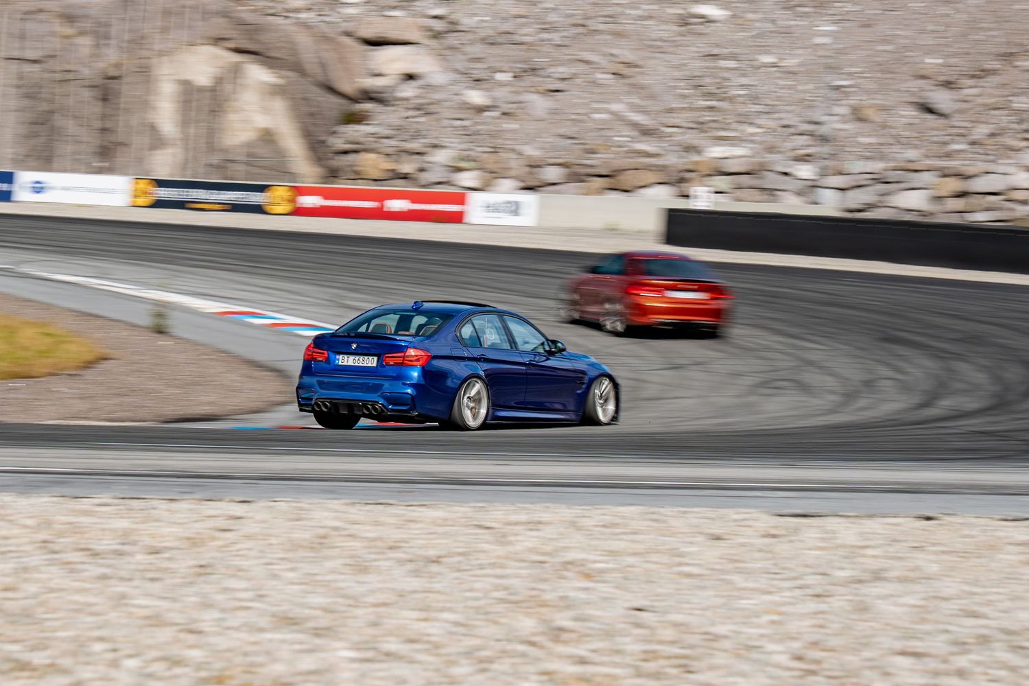 A bright blue BMW M3 sports car races around a curving racetrack against a desert mountain backdrop.