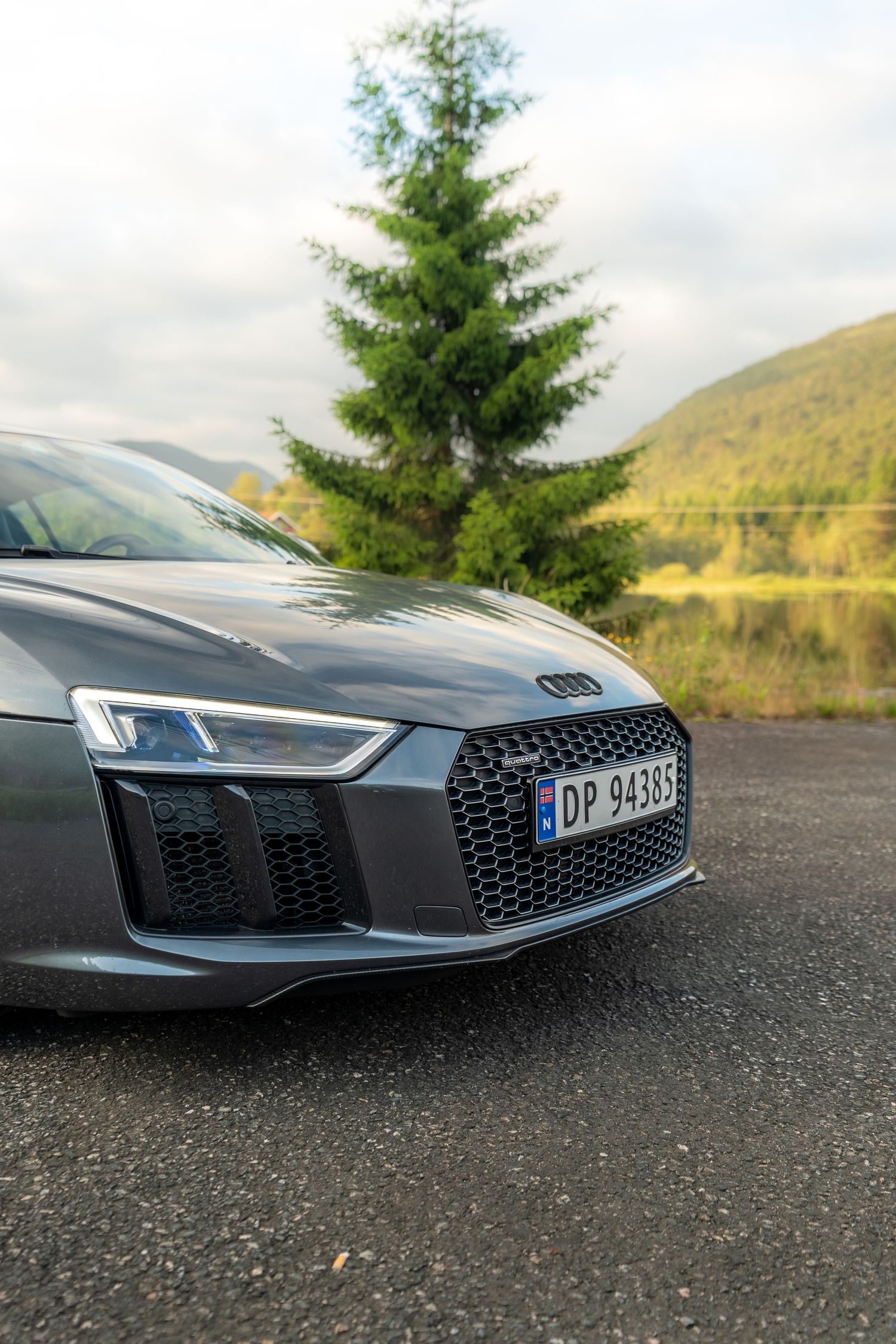 Close-up detail shots of a dark Audi R8's front grille and headlights against a natural backdrop.