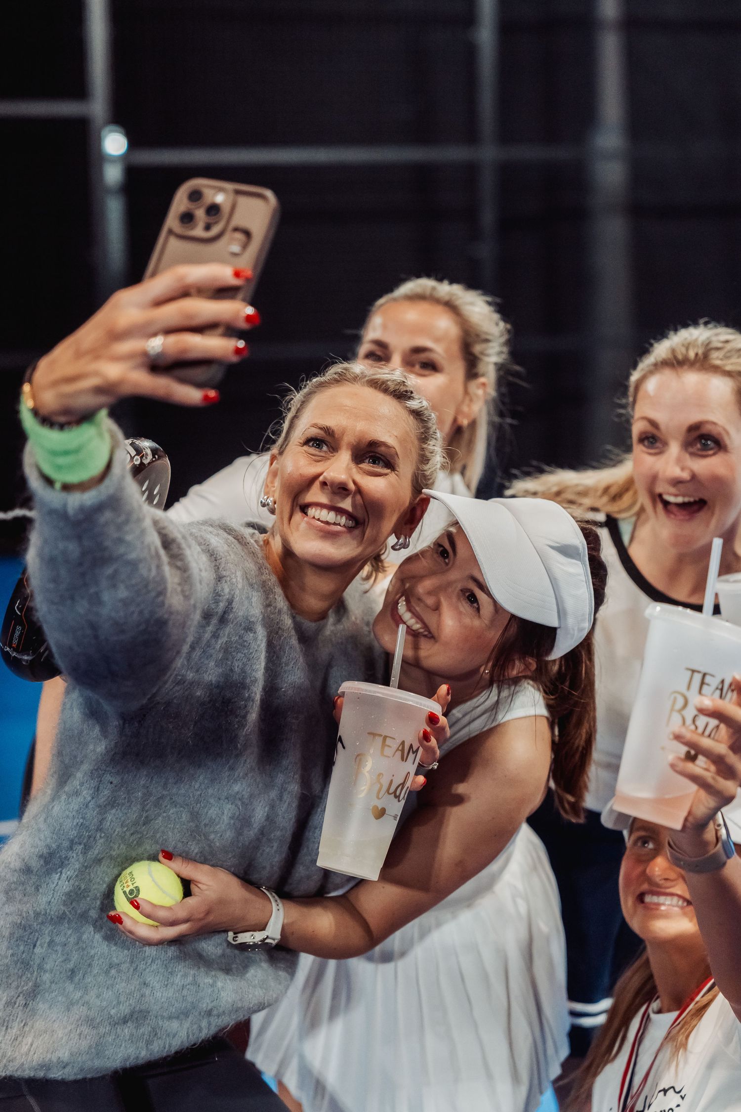 Group taking selfie with tennis ball and drinks after match.