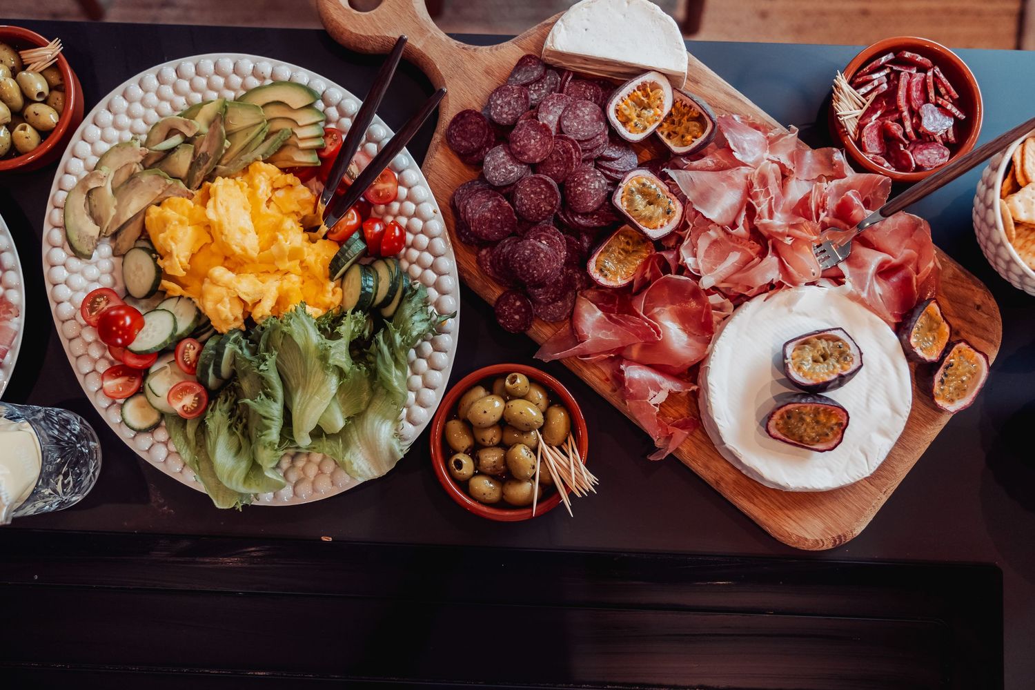 Multiple plates of colorful Mediterranean food and appetizers arranged on a dark rustic wooden table from above.