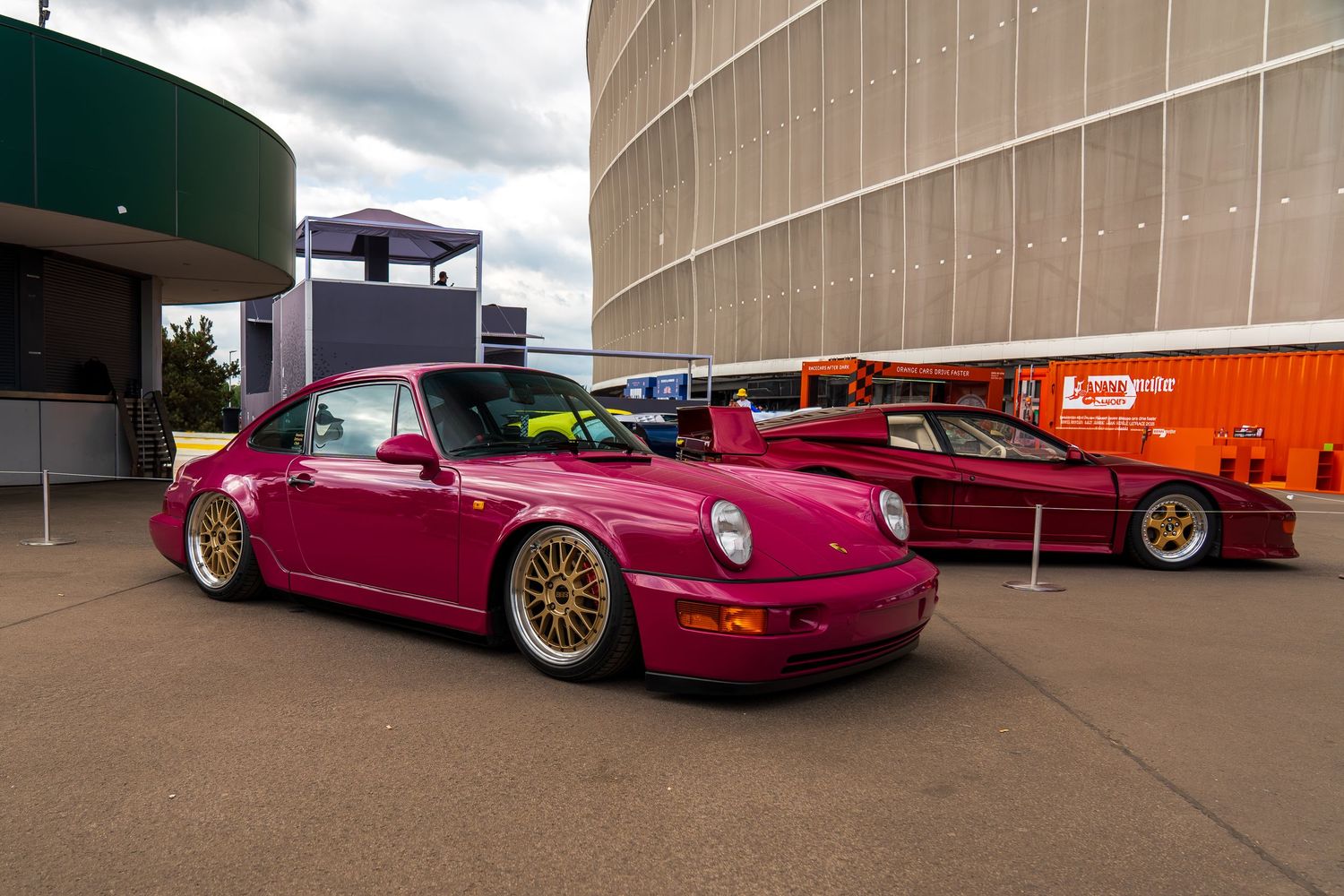 Line of modified luxury cars parked against industrial building exterior.