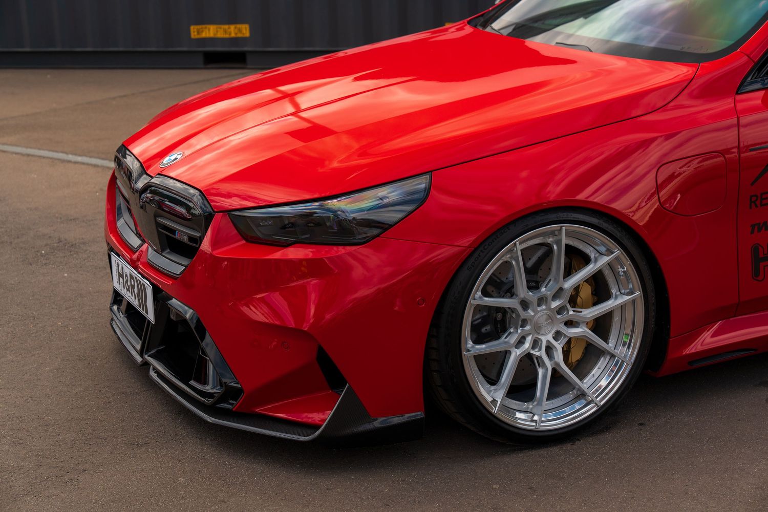 Close-up of a red BMW M car's front quarter panel with custom wheels and carbon fiber trim.