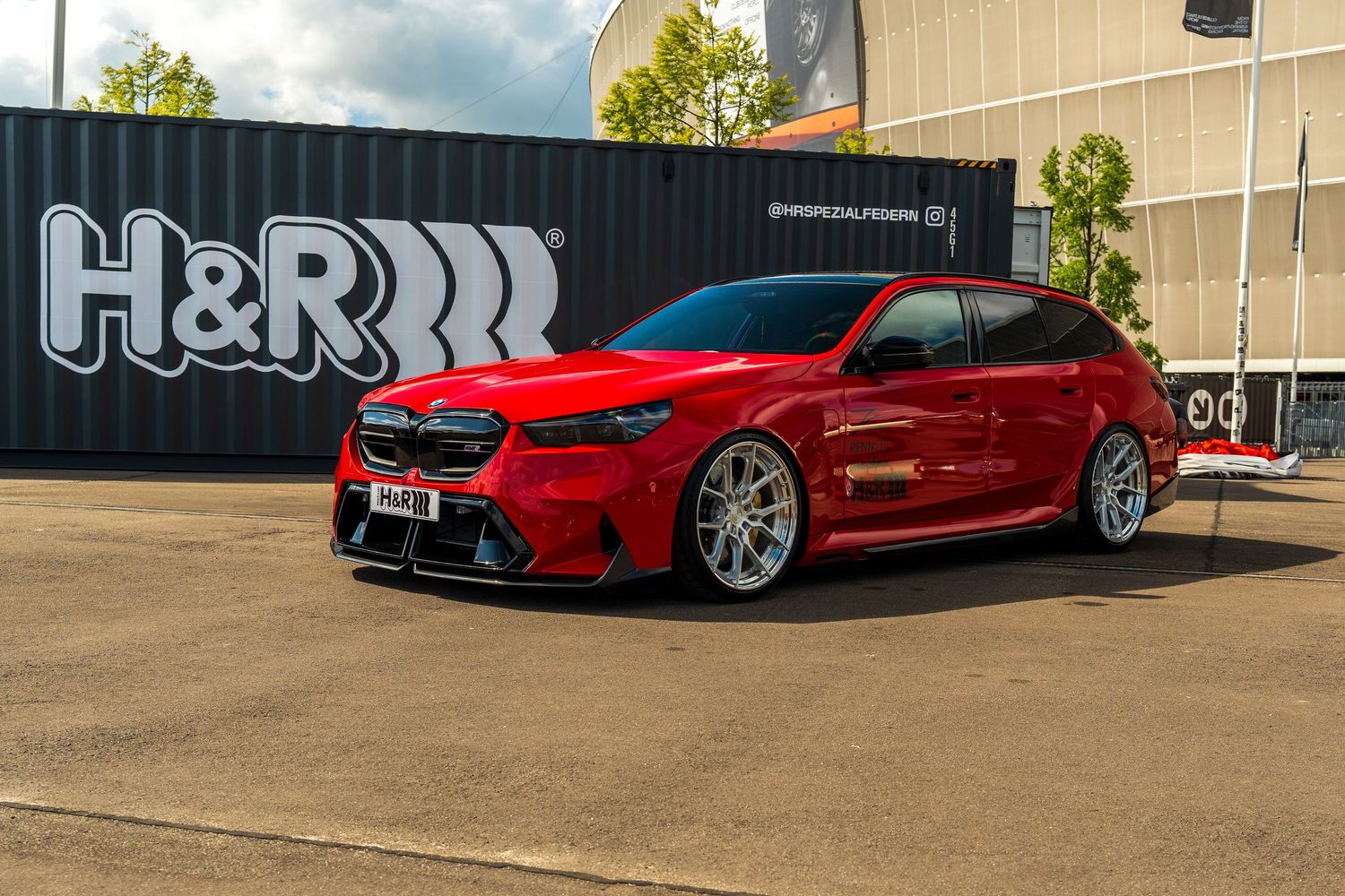 Modified red Kia Stinger GT with lowered suspension parked in front of H&R Springs signage.