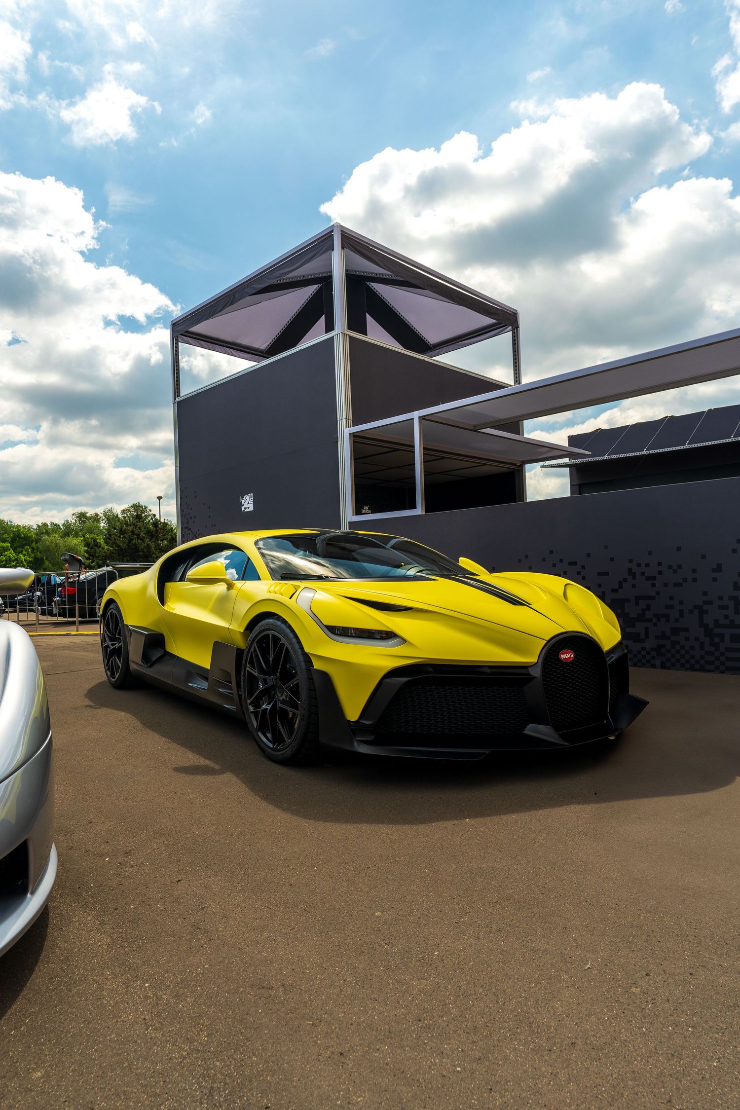 Yellow McLaren supercar showcased at an outdoor event with dramatic cloud-filled sky.