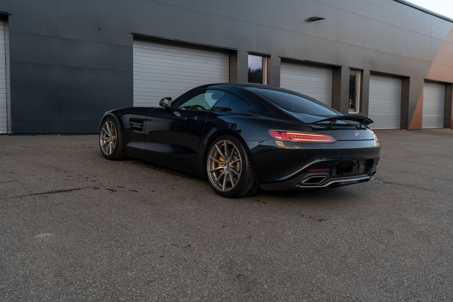 Black Mercedes AMG GT sports car with bronze wheels parked in front of industrial garage doors.