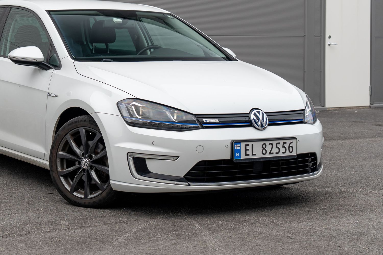 A white Volkswagen Golf GTI parked in front of a grey concrete wall shows its aggressive front-end styling.