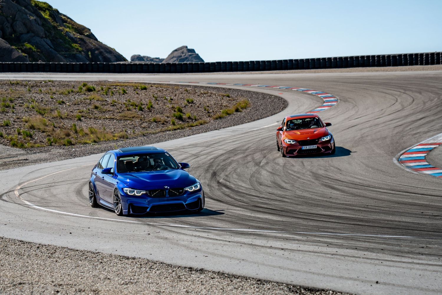 Two sports cars, one blue and one red, racing around a curved track on a mountainous circuit.