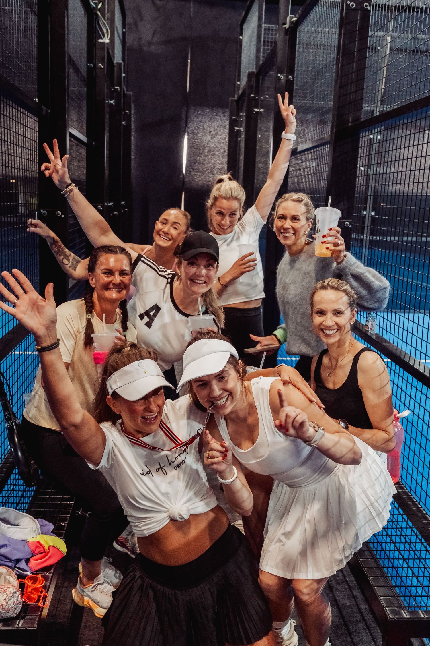 Group of players celebrating together on indoor tennis court showing victory signs.