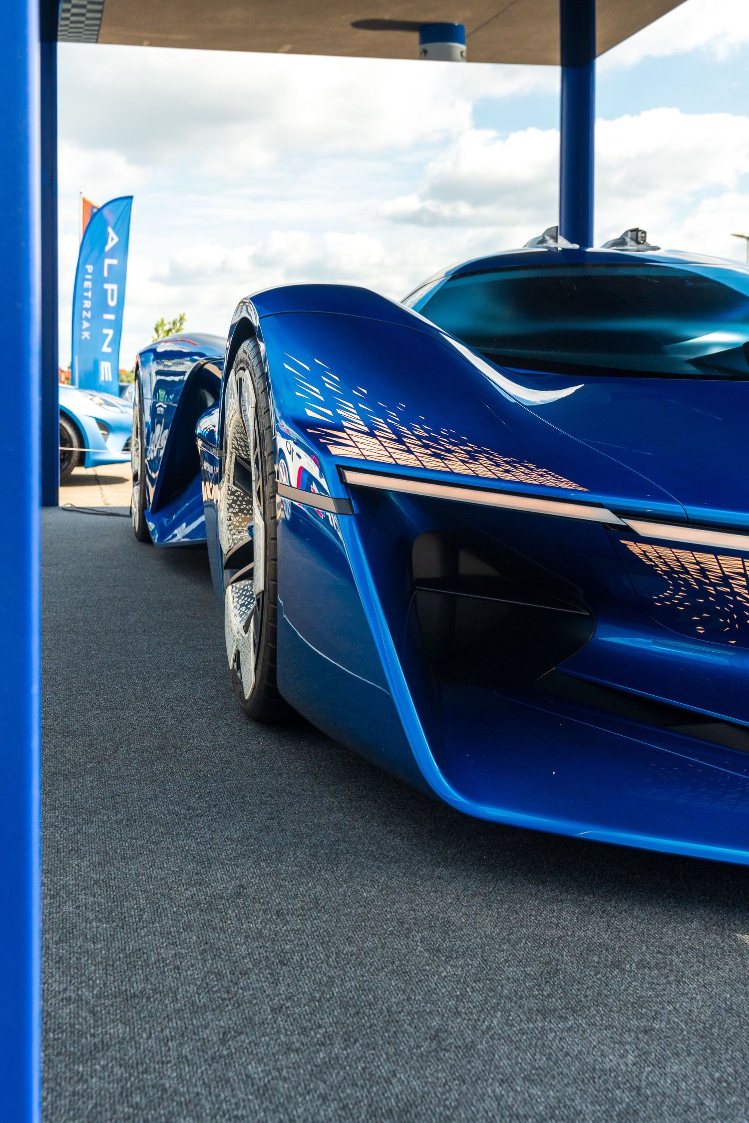Sleek blue concept car with aerodynamic design and futuristic styling features displayed under covered parking.