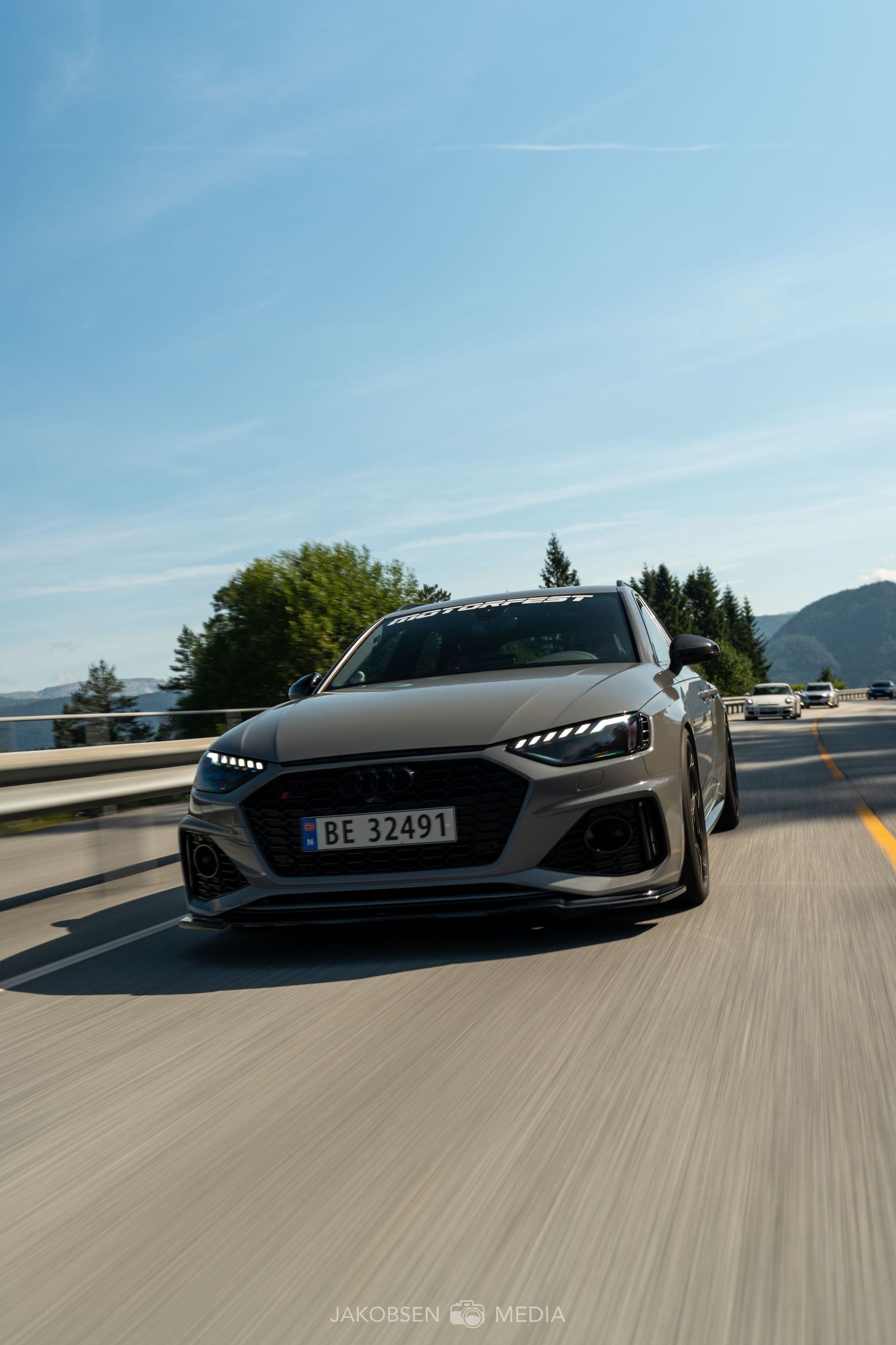 Gray Audi RS car photographed in motion on mountain road against blue sky.