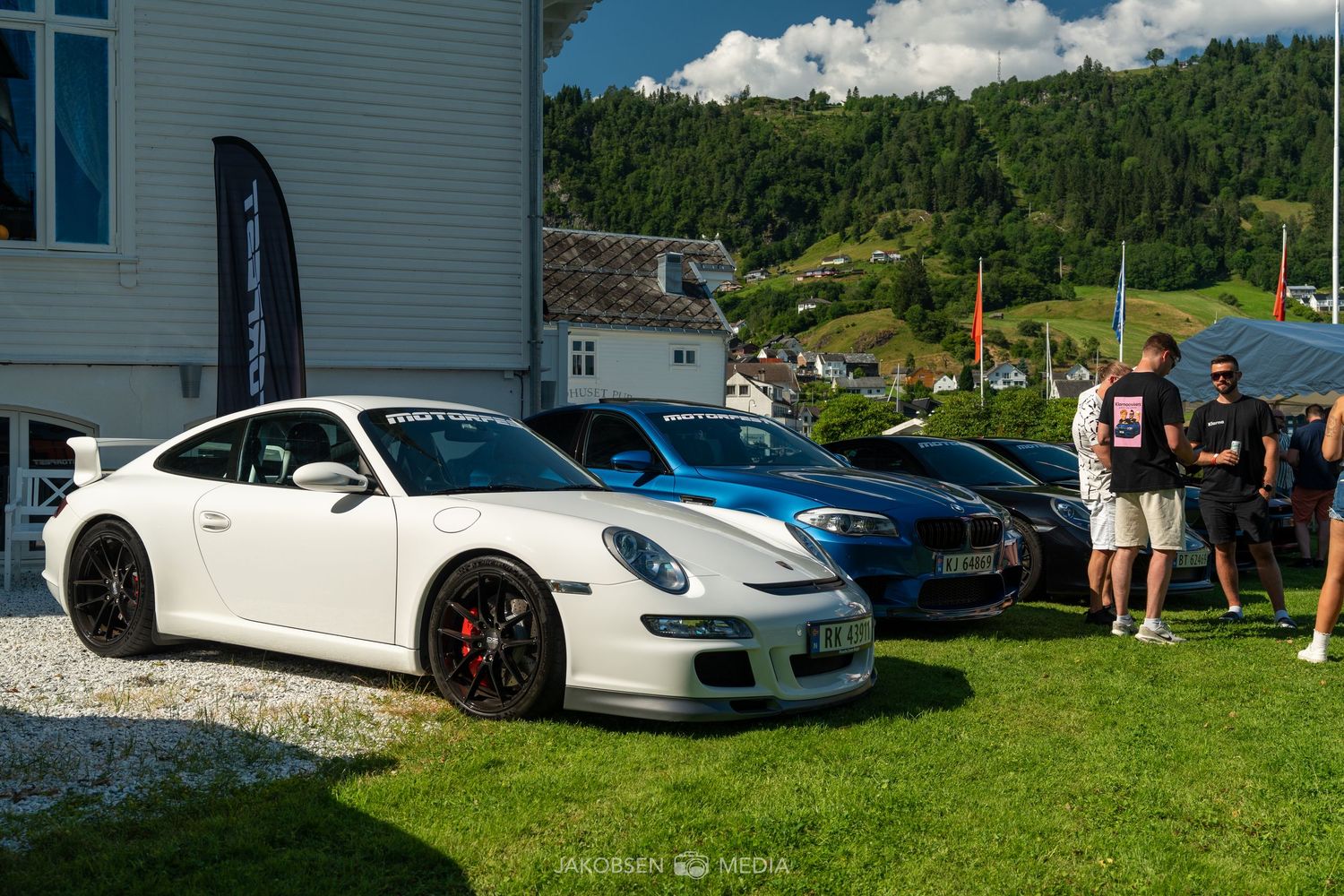Luxury sports cars parked on grass with mountains and blue sky in background.
