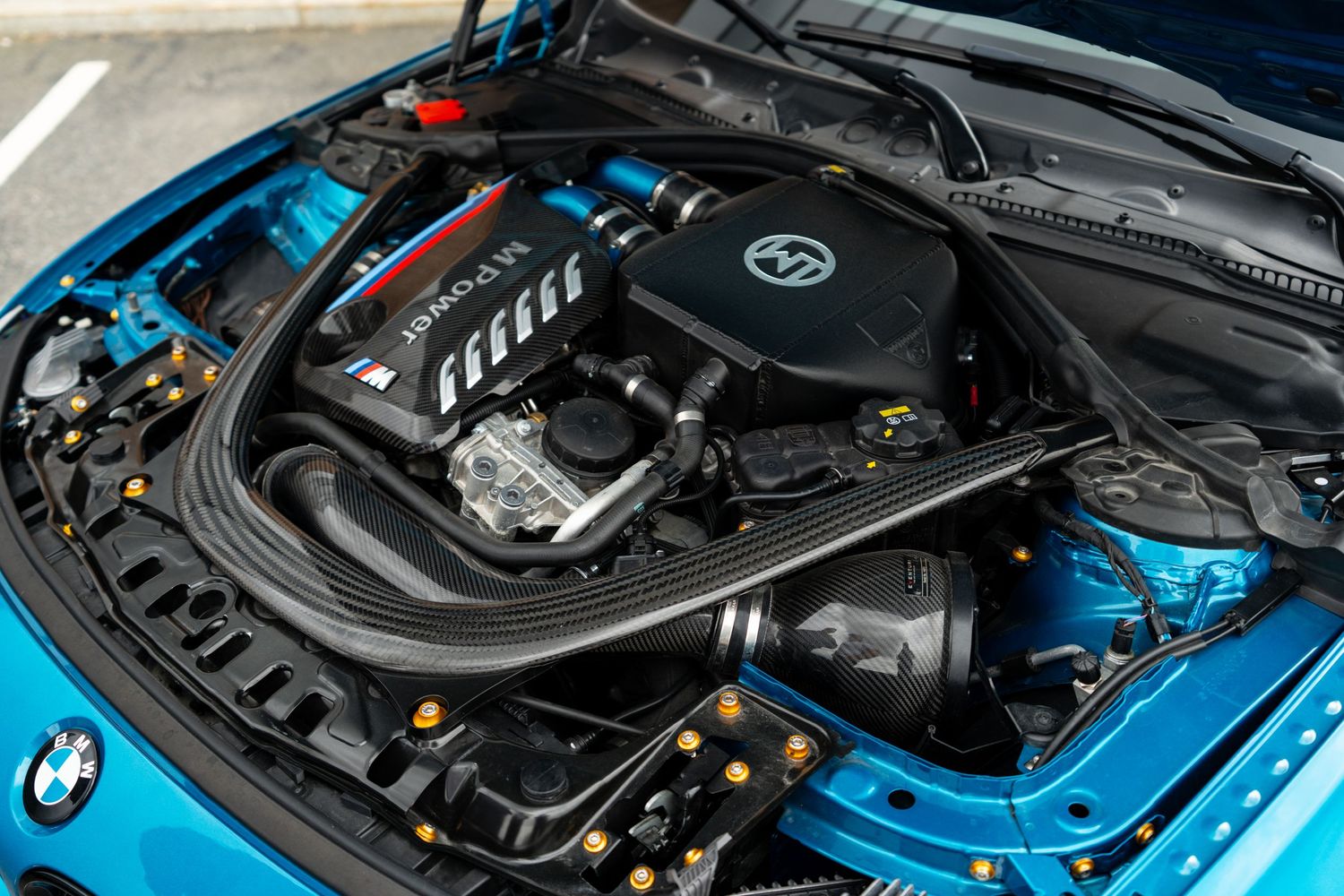 Under the hood of a BMW M3 showing the performance engine bay and blue exterior paint.