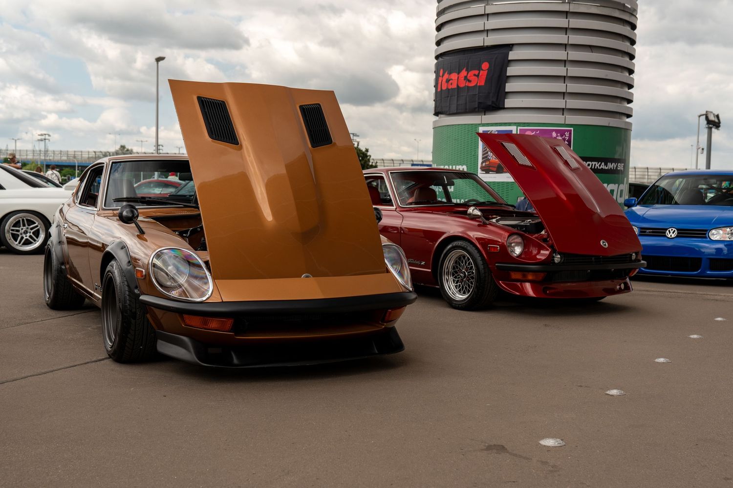 Classic brown Datsun Z and red sports car displayed at outdoor car show.