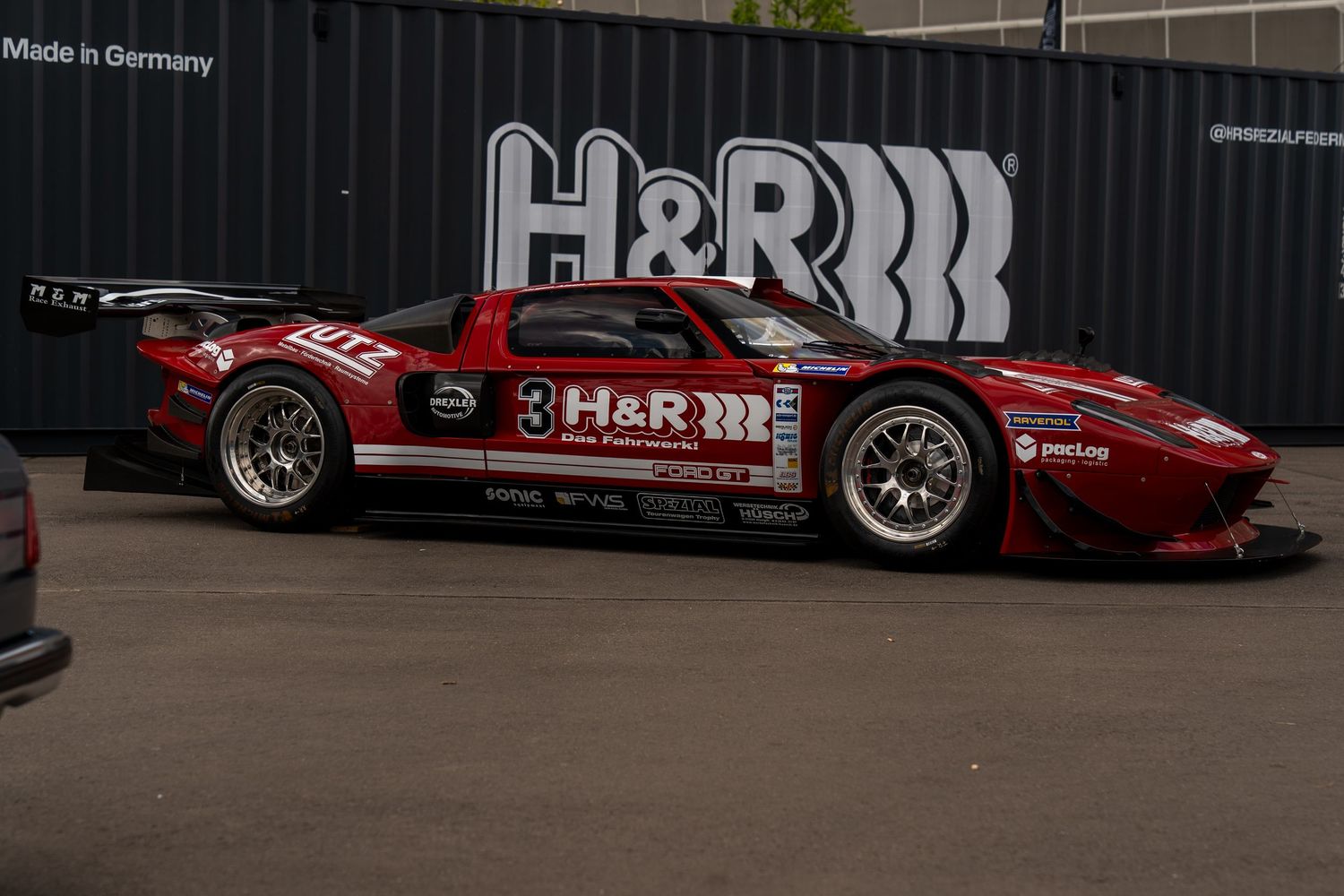 Red racing cars with H&R sponsorship displayed against black wall with branded graphics.