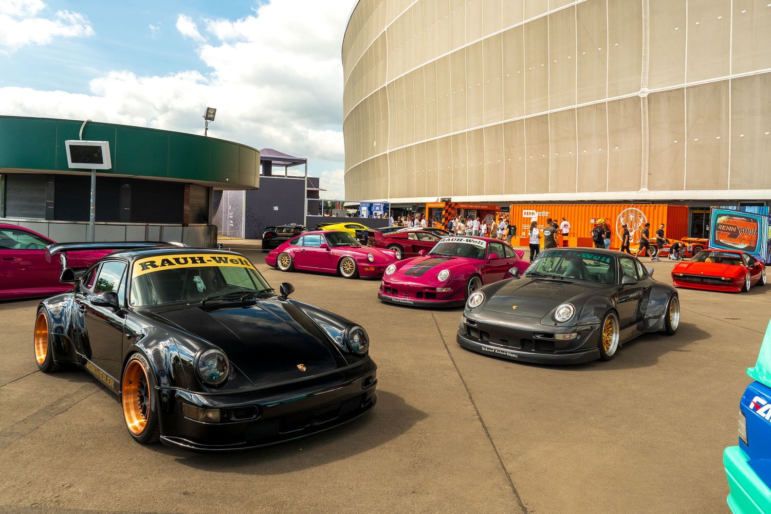 High-end sports cars including modified Porsche 911s and custom vehicles displayed at an outdoor car show event.