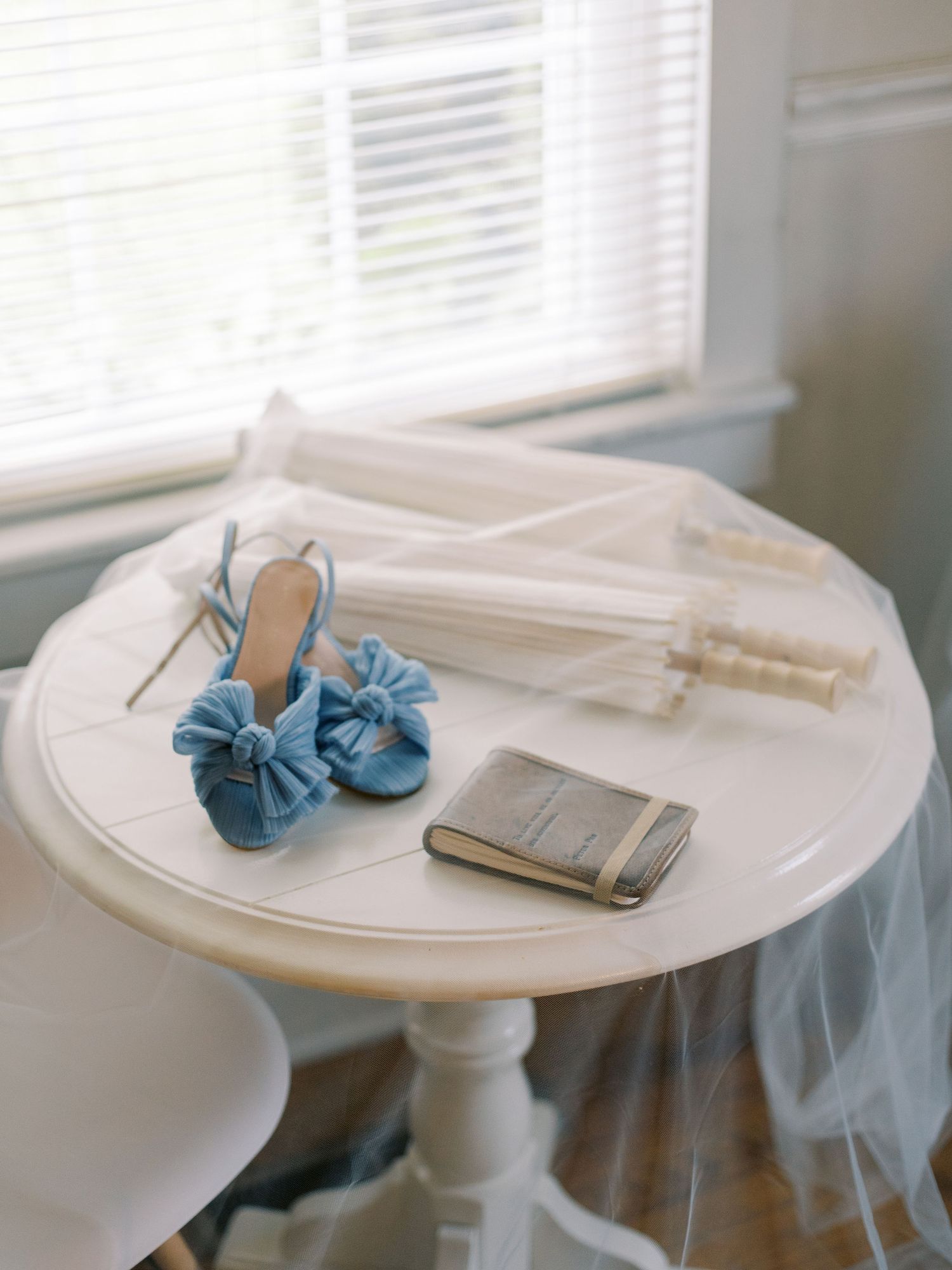 Wedding accessories including blue shoes and veil arranged on a white round table.