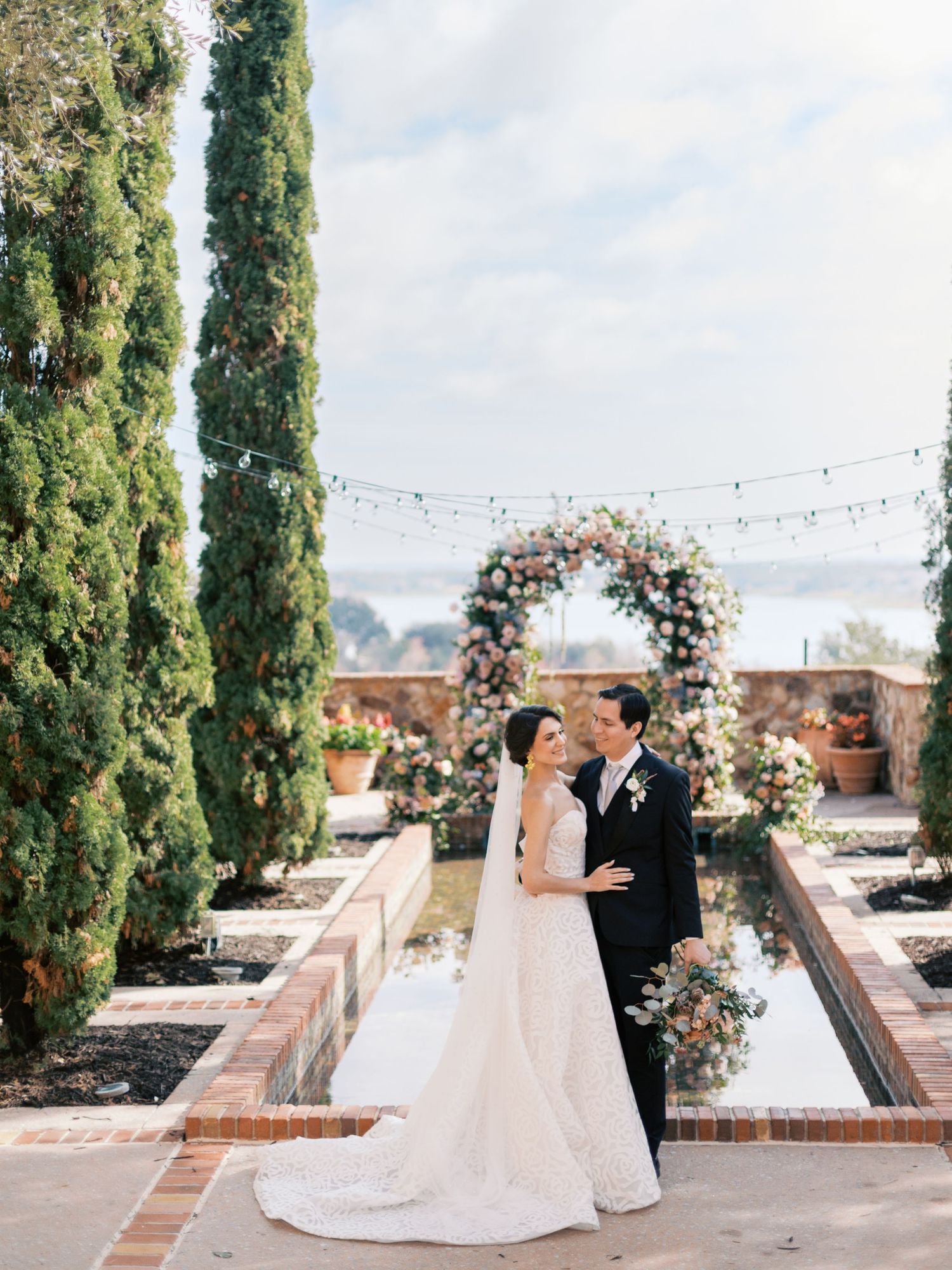 Elegant wedding ceremony setup with floral arch and cypress trees in an outdoor courtyard.