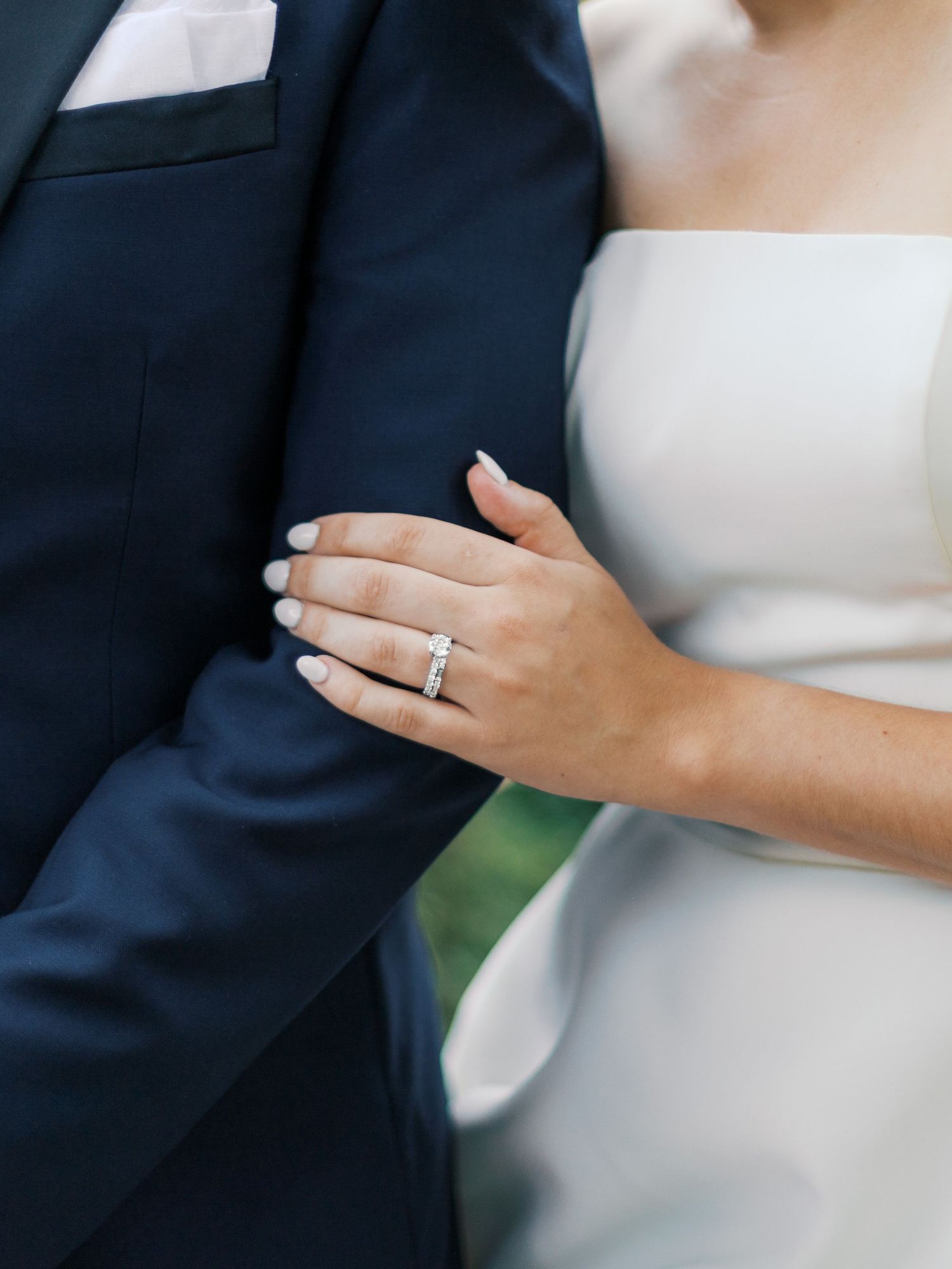 Close-up of diamond engagement ring and white dress against navy suit.