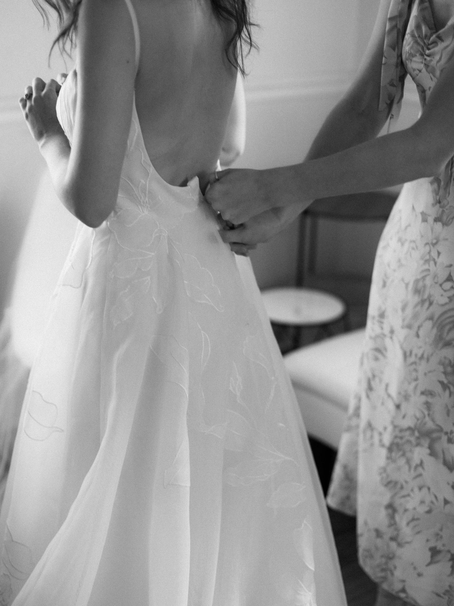 Black and white photo of a wedding dress being buttoned up.
