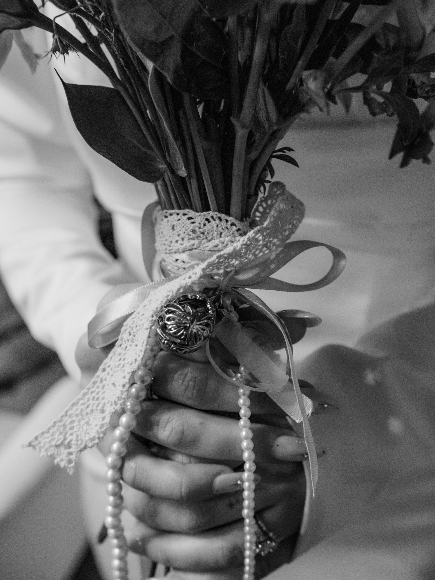 Close-up of hands holding bridal bouquet wrapped in lace and pearls in black and white.