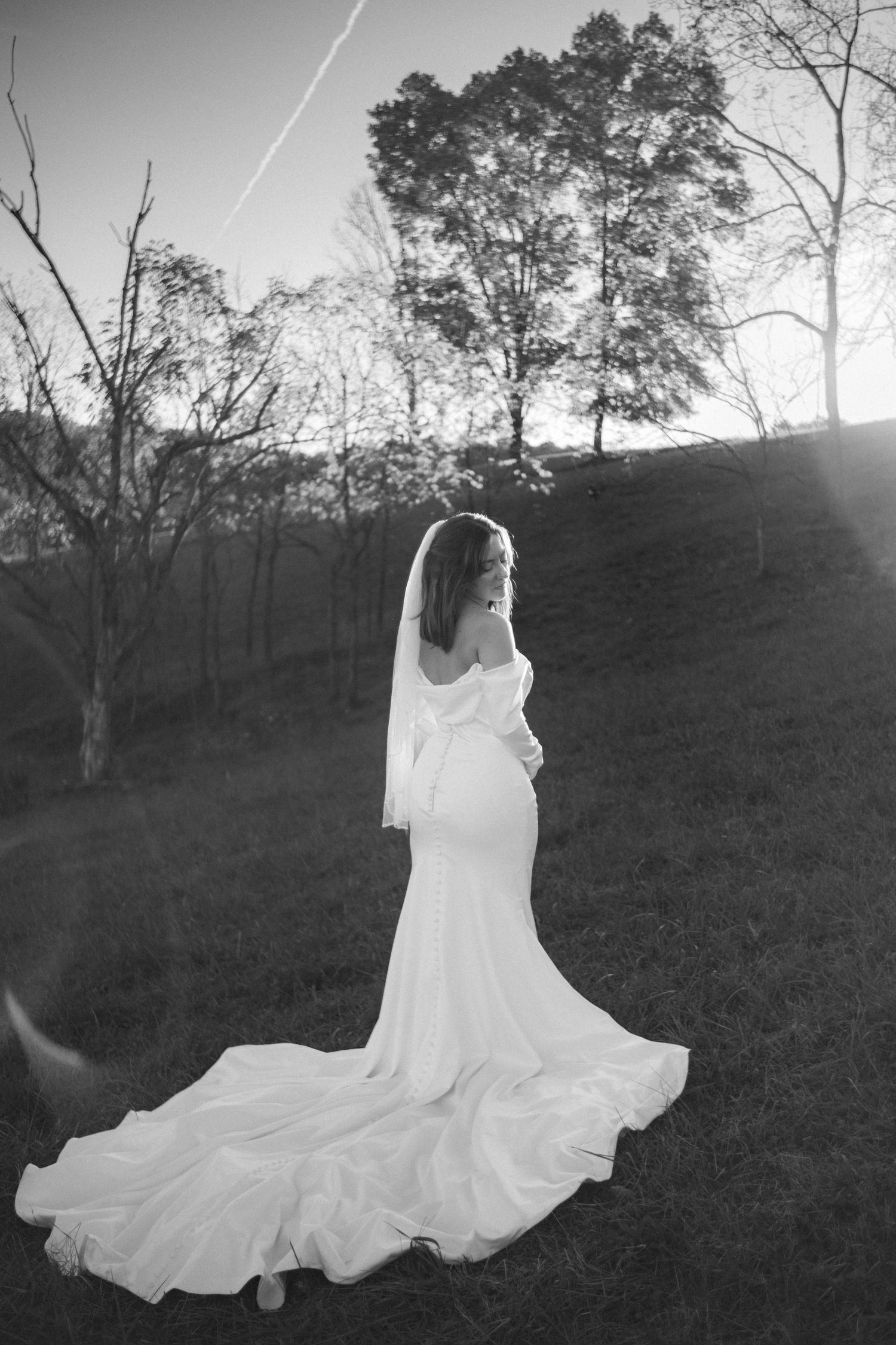 Dramatic black and white portrait of flowing wedding dress against sunset landscape.