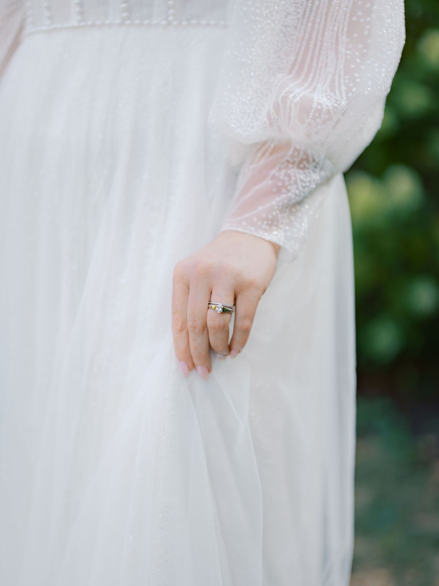 Close-up of a bride's hand wearing an engagement ring against her white lace dress.